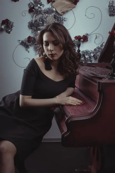 Hezká mladá model v černých šatech poblíž red piano — Stock fotografie