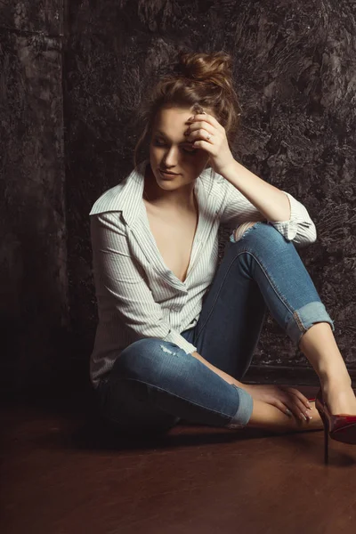 Τρυφερή νεαρή γυναίκα στο πουκάμισο και τζιν που κάθεται στο πάτωμα — Φωτογραφία Αρχείου
