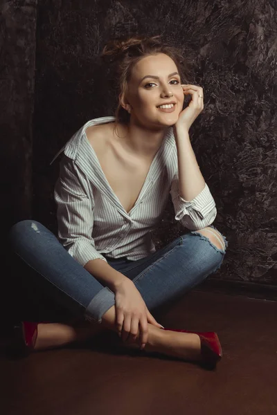 シャツとジーンズを床に座って幸せな若いモデル — ストック写真