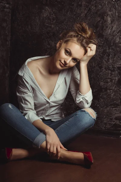 Ελκυστική νεαρή γυναίκα στο πουκάμισο και τζιν που κάθεται στο πάτωμα — Φωτογραφία Αρχείου