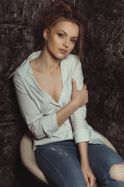 Maravillosa joven modelo sentada en una silla con rayas y jeans — Foto de Stock