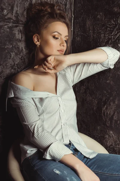 Прекрасная молодая модель сидит на стуле в полосатых и порванных джинсах — стоковое фото