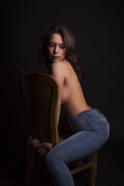 Giovane donna in topless in jeans blu seduta su una sedia in studio — Foto Stock