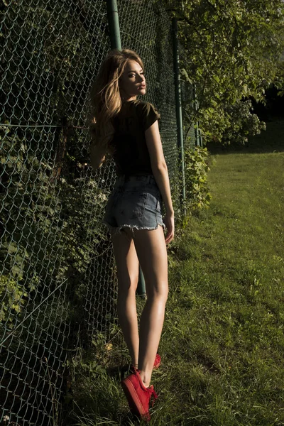 Vacker ung modell som poserar på rutnätet staketet i eleganta kläder — Stockfoto