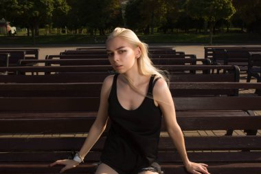 R bir bankta poz şık giysiler içinde güzel sarışın model