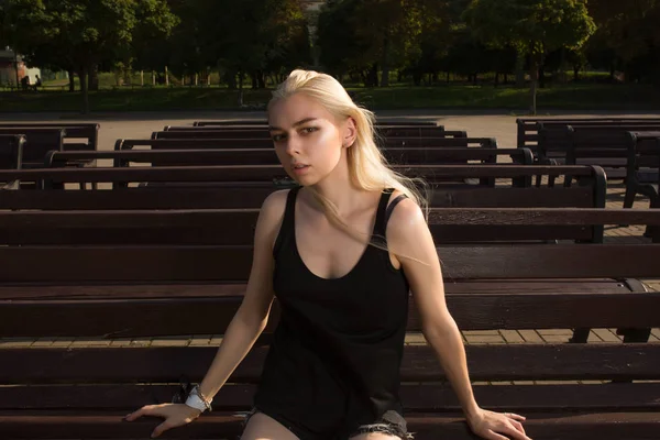 R bir bankta poz şık giysiler içinde güzel sarışın model