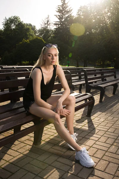 Bonita modelo rubia en ropa casual posando en un banco en soleado — Foto de Stock