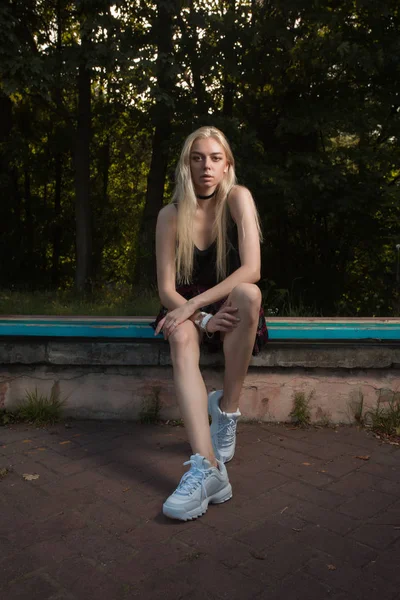 Vacker ung modell med långa blonda hår poserar på en bänk i — Stockfoto