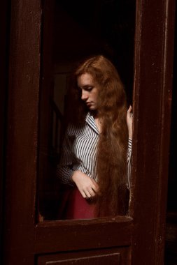 Kapalı bir cam kapının arkasında duran görkemli kırmızı saçlı model. R