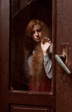 Şehvetli kırmızı saçlı model ayakta kapalı cam kapının arkasında. Ra
