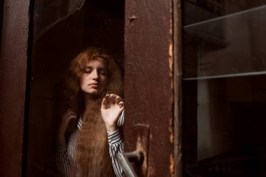 Çekici kırmızı saçlı model ayakta kapalı cam kapının arkasında.
