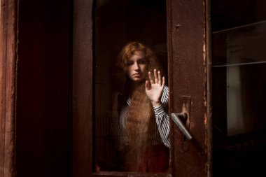 Güzel kırmızı saçlı model ayakta kapalı cam kapının arkasında. 