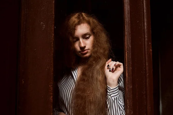 Jovem modelo de cabelos vermelhos tristes com cabelos longos em pé atrás de um clos — Fotografia de Stock