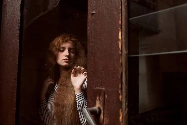 Atraktivní červené vlasy model stojící za uzavřené skleněné dveře. — Stock fotografie