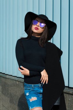 Lüks genç modeli moda ceket, yırtık kot pantolon ve şapka takıyor. Kadını
