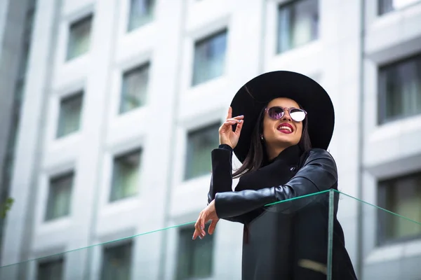 Felice donna bruna indossa occhiali e cappello per strada. Città l — Foto Stock