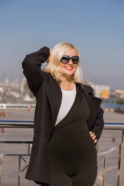 Uśmiechnięta Blondynka modelu pozowanie w czarny płaszcz nosi okulary i p — Zdjęcie stockowe