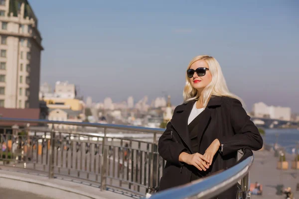Ελκυστική ξανθιά μοντέλο που θέτουν σε μαύρο παλτό φοράει γυαλιά ηλίου για — Φωτογραφία Αρχείου