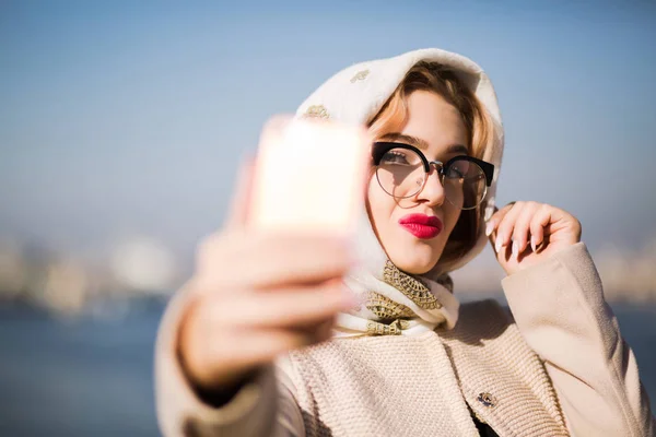 Kaunis nuori nainen ottaa selfie älypuhelimella. Nainen pukeutuu s — kuvapankkivalokuva