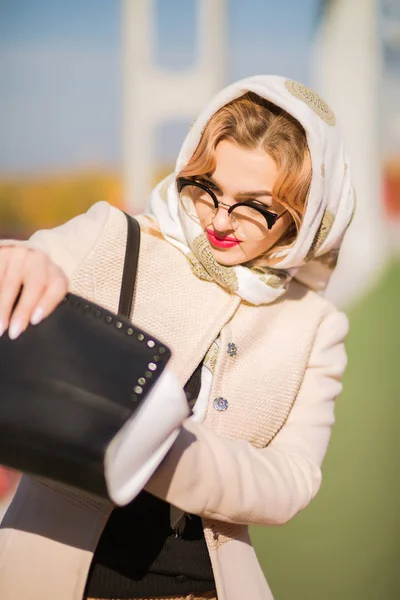 Stylish dressed model looking into her handbag , wears beige coa — Stock Photo, Image