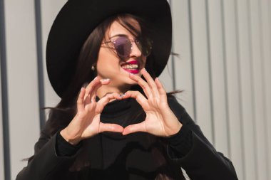 Siyah şapka ve güneş gözlüğü kalp gösterilen genç çekici model