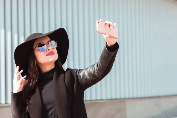 Stylish brunette model wears fashionable hat and sunglasses, tak — Stock Photo, Image