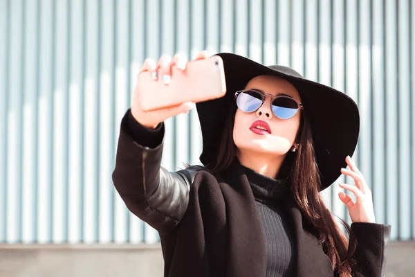 Moderiktigt klädd kvinna bär hatt och solglasögon, tar själv — Stockfoto