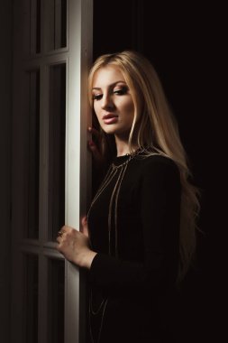 Siyah elbiseli, uzun dalgalı saçlı, narin sarışın kadın. 