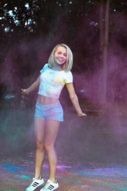 Neşeli sarışın kadın etrafında patlayan Holi Tozu ile atlama 