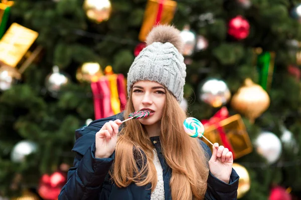 Attractive blonde girl in knitted warm hat eating colorful Chris — Stock Photo, Image