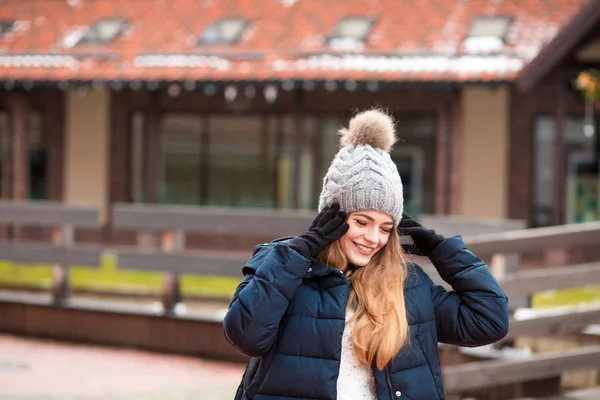 Cheerful young woman in knitted hat and coat posing near the hou — Stock Photo, Image
