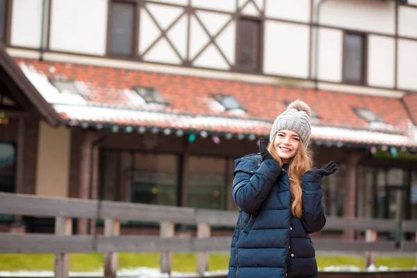 Stylish young woman in knitted hat and coat posing near the hous — Stock Photo, Image