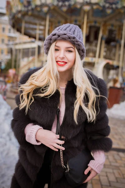 Feliz jovem mulher vestindo chapéu de malha e casaco de pele, posando perto — Fotografia de Stock