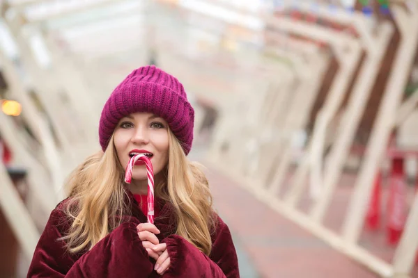 Increíble mujer rubia en sombrero de punto rojo posando con bastón de caramelo a — Foto de Stock