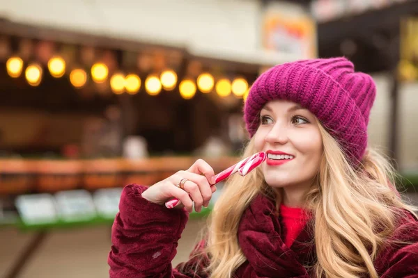 Adorable blonde girl in red knitted hat posing with candy cane a — Stock Photo, Image