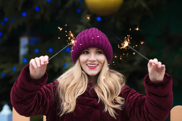 Joyful blonde woman dressed in red knitted hat and warm coat hol — Stock Photo, Image