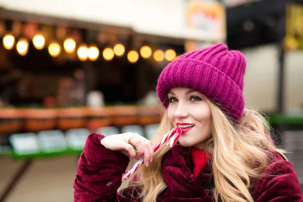 Cheerful blonde girl in red knitted hat posing with candy cane a — Stock Photo, Image