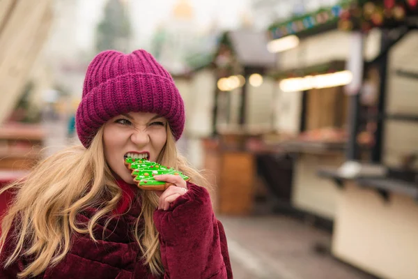 Funny young woman eating delicious christmas gingerbread at the — Stock Photo, Image
