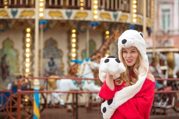Emotionale blonde Frau mit lustigem Hut posiert neben Karussell-Witz — Stockfoto