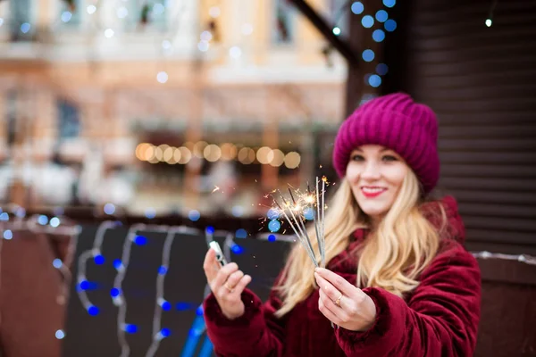 Cheerful blonde girl holding glowing Bengal lights at the Christ — Stock Photo, Image