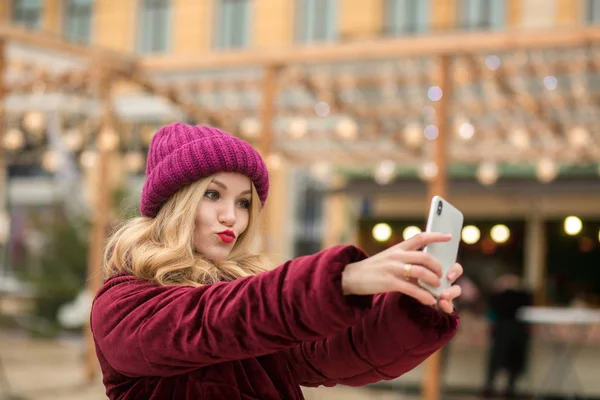 Freudige blonde Frau in warmen Kleidern macht Selfie an der — Stockfoto