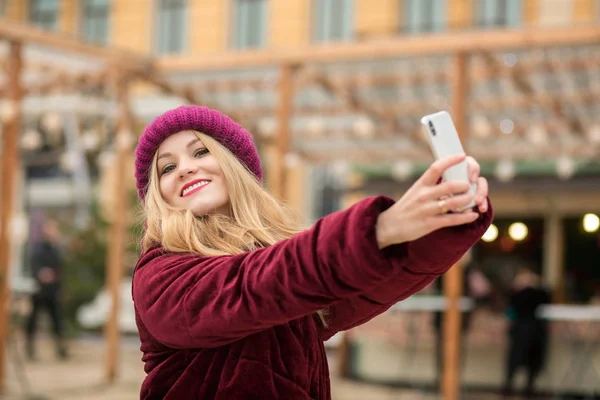 Merry blonde woman dressed in warm clothes making selfie at the — Stock Photo, Image