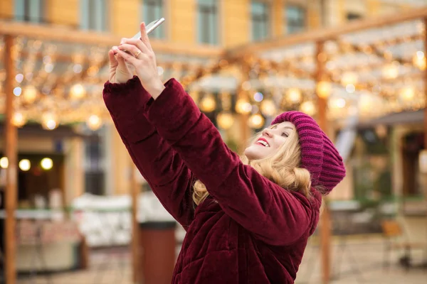 Glückliche blonde Frau in warmen Kleidern macht Selfie an der — Stockfoto