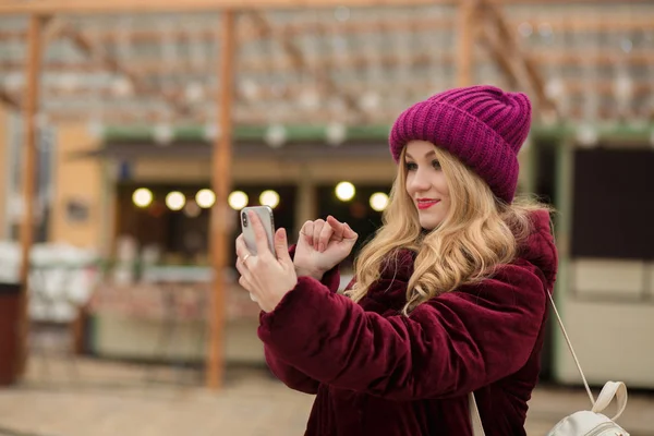 Kaunis blondi nainen kirjoittaa viestin matkapuhelimeen, seisoo — kuvapankkivalokuva