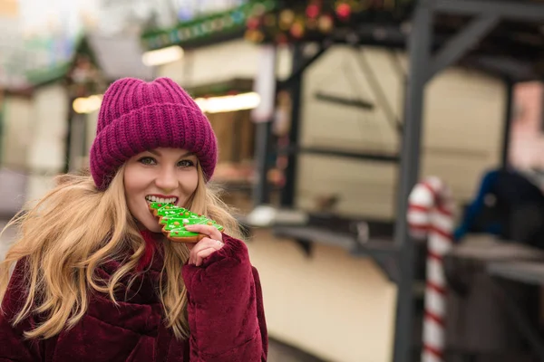 Happy young woman eating delicious christmas gingerbread at the — Stock Photo, Image