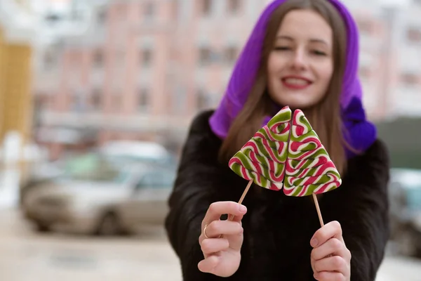 Cheerful young model wearing winter outfit, holding caramel swee — Stock Photo, Image