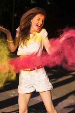 Pembe kuru boya Holi bulutu içinde poz neşeli esmer kadın