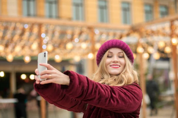 Mulher loira alegre vestida com roupas quentes fazendo selfie em t — Fotografia de Stock