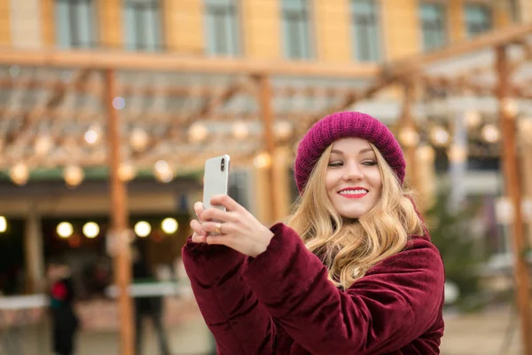 Mulher loira atraente vestida com roupas quentes fazendo selfie um — Fotografia de Stock