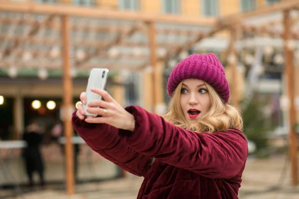 Εκφραστική ξανθιά γυναίκα, ντυμένη με ζεστά ρούχα, καθιστώντας selfie στο — Φωτογραφία Αρχείου